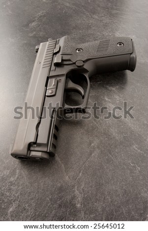 Black semi automatic hand gun or personal defense pistol on black textured surface.
