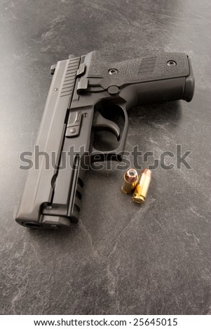 Black hand gun or semi automatic pistol on black textured surface with hollow point personal defense bullets.