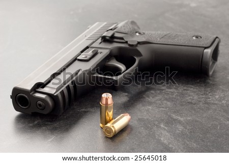 Black hand gun or pistol on black textured surface with hollow point personal defense bullets.