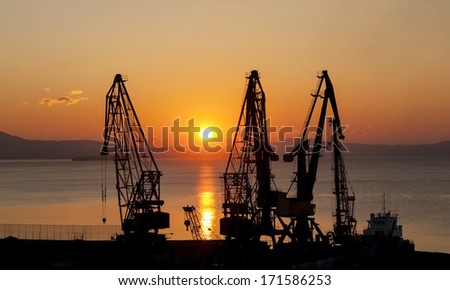 Silhouettes of port cranes on a background of a rising sun