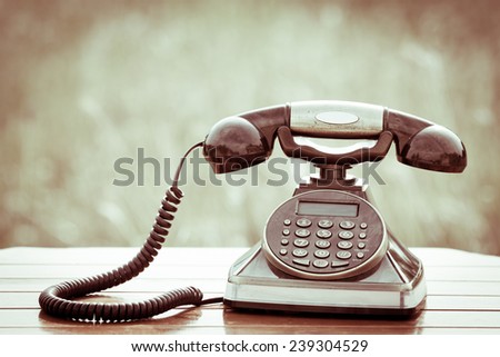 Old vintage telephone on wood table on meadow background in retro style