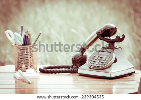 Old vintage telephone with stationery on wood table on meadow background in retro style