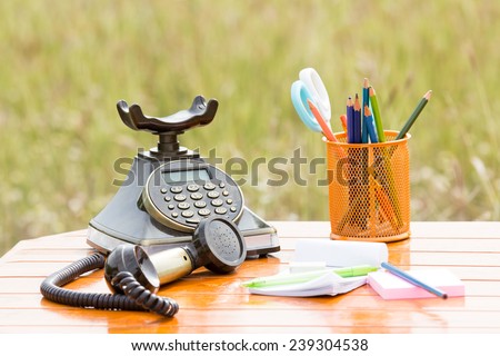 Old vintage telephone with stationery on wood table on meadow background in retro style
