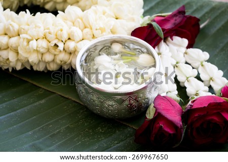water with jasmine flower in silver bowl and jasmine garland on banana leaf background
