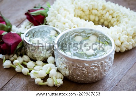 water with jasmine flower in silver bowl and jasmine garland on wooden background