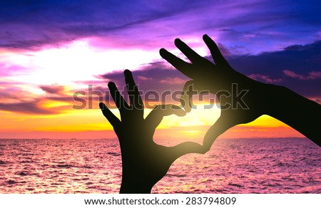 Silhouette hand in heart shape on sunset over the sea