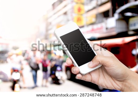 woman hand hold smart phone, tablet,cellphone on blur traffic and people in big market background