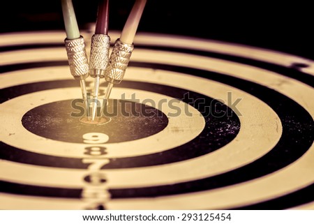 Success hitting target aim goal achievement. Three darts in target center on dartboard, vintage effect filter