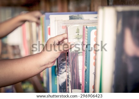 hand of little girl selecting a book from book shelf in vintage color tone