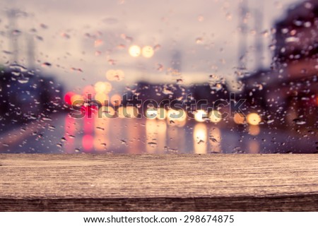 wooden table with blur traffic view through a car windscreen covered in rain for background