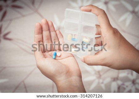 woman hand pouring pills from a pill reminder box into her hand