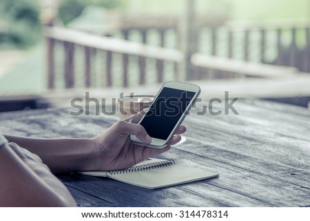 Women hand using smartphone,cellphone,tablet over wooden table in vintage color filter
