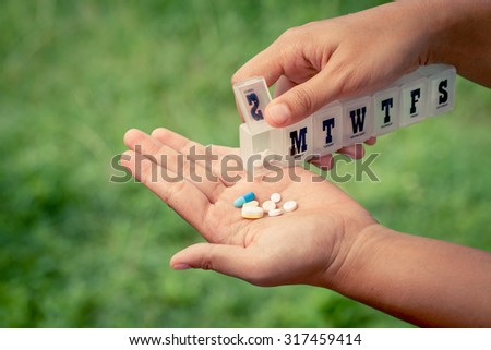 woman hand pouring pills from a pill reminder box into her hand on green nature background in vintage filter