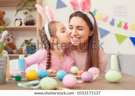 Mother and daughter together at home easter preparation in bunny ears sitting girl kissing mom