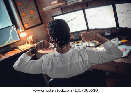 Rear view at stock trader broker stretching hands at workplace