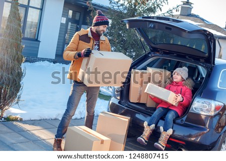 Fsther and daughter moving to new apartment together during winter standing outdoors near car taking boxes from trunk smiling happy