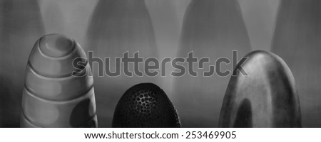 Black and white image of three eggs made of different materials shrouded into the strange light of its mysterious background.