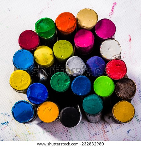 Multie colored oil pastels standing up right in a group or bundle and situated on white art paper that has been marked all over by the  colored oil pastels.