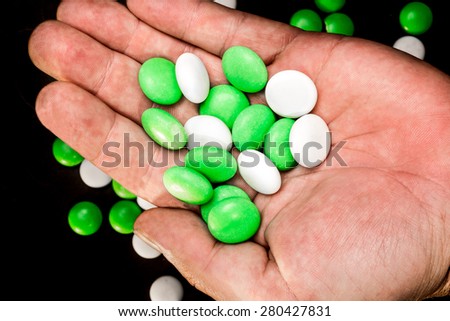 A hand holding several green and white mints in the palm while some more mints lie on the black background.