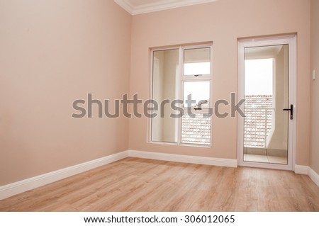 An Empty bedroom of a newly build house with laminated floor and glass windows and door that lead out to the patio.