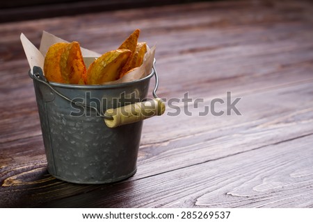 Roast potatoes in a bucket on a wooden background.