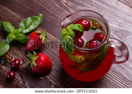 Glass jug of freshness lemonade with strawberries and cranberry on wooden background.