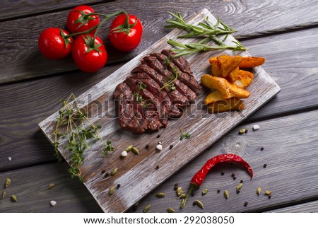 Delicious beef steak with tomatos. Meat and rosemary on wooden background.