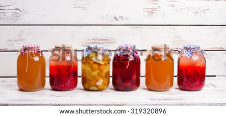 Canned fruit drinks in glass jars. Natural juices are on old wooden shelf.
