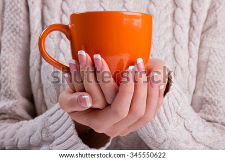 Woman holds a winter cup close up. Woman hands with elegant french manicure nails design holding a cozy mug. Winter and Christmas time concept.
