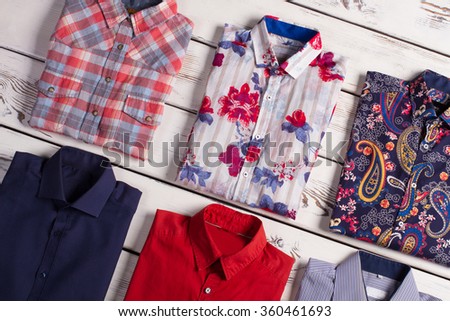 Many different bright stylish men\'s shirts with different colors and prints on old wooden background.