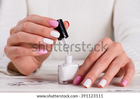 Girl paints her nails white nail polish. Beauty salon. White-pink knitted manicure.