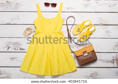 Collection of women\'s summer clothes. Yellow bright dress with accessories on wooden background.