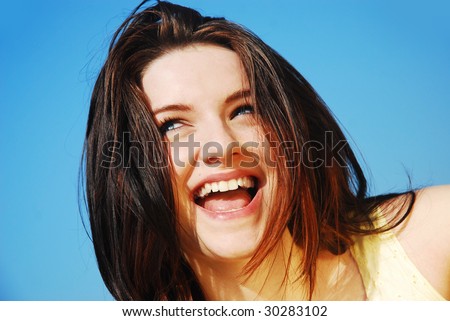 A young woman laughing in front of a blue sky.