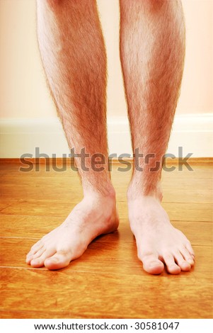 A man\'s naked legs standing on a bath mat.