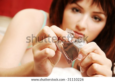 A beautiful young woman opening a condom on her bed. Focus on the condom in the foreground.