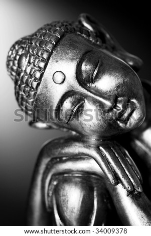 A black and white image of a Buddha statue resting, in front of a dark background.