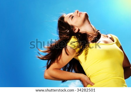 A beautiful young woman throwing her head back in the sun outdoors in front of a blue sky.