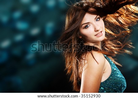 A beautiful young brunette woman dancing with her hair in motion in a nightclub scene.