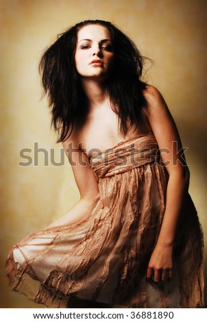 A beautiful young brunette woman posing holding her dress. Dramatic lighting, romantic feel.