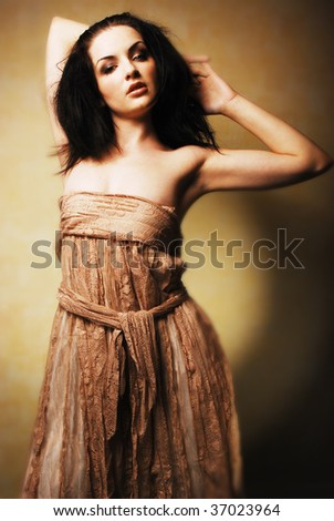 A beautiful young brunette woman posing with her arms up. Dramatic lighting, romantic feel.