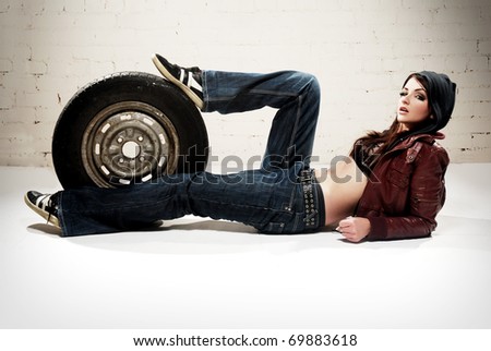 A ghetto styled girl posing in front of brick wall with a wheel