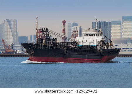 An old medium sized dredging ship cruises across the bay of a large city.