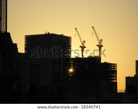 Two skyscraper construction cranes in a silhouette against the yellow sky of a sun setting