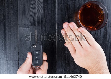 Car key and whiskey alcohol drink in a glass on black wooden table. Don\'t drink and drive abstract concept.