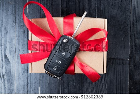 Car key on a paper box with red ribbon bow on black natural wooden table background. Christmas or Valentine\'s Day gift or present abstract concept.
