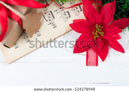 Christmas ornament and music sheet on white natural wooden table. Red ribbon bow. Poinsettia. Copy space at the bottom. Gift or present with label and twine.