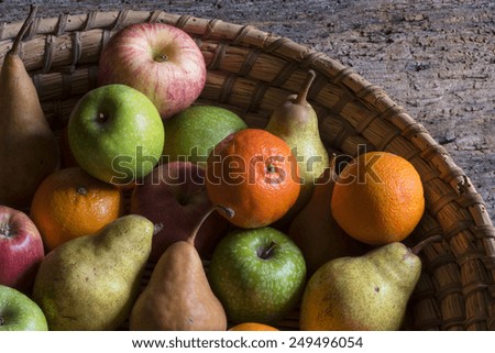Assortment of fruits on in a basket ,various fruits from the garden in an old wicker basket , apples, pears, orange,mandarin , natural light, photo from above