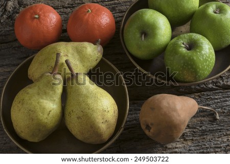 mixed fruits dish in brass,various fruit of the garden in two plates of brass laid on an old wooden table. pears, apples, orange, mandarin, natural light