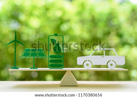 Eco friendly car / green renewable energy, save earth and nature concept : Windmill or wind turbine, solar energy panel, dried cell battery and leaf, white sedan car on a seesaw / simple balance scale