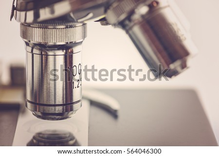Close up view of objective lenses with a clear glass microscope slide on a black stage and clip. A microscope is an instrument used to see objects that are too small for the naked eye. Science concept